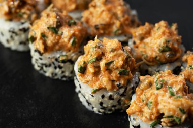 Somon, avokado, midye ve siyah susam tohumlu taze suşi ruloları siyah bir taş levhada servis edilir. Japon suşi uramaki ya da California dürümü. Kapat.