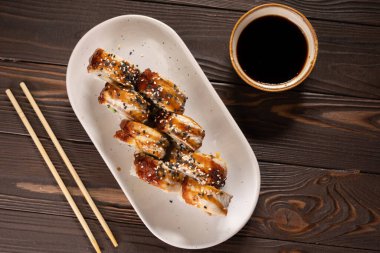 Yılanbalıklı suşi. Kanada mı? Ahşap arka planda yemek çubuklarıyla bir tabakta, üst manzara. Boşluğu kopyala