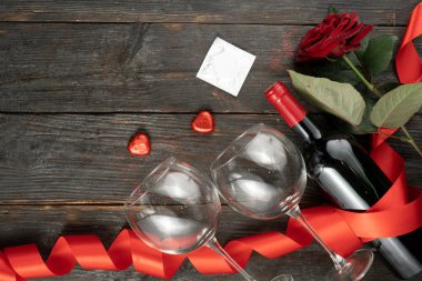 Sevgililer gününde şarap şişesi, prezervatif, gözlük, kalp şeklinde şekerler, ahşap arka planda kırmızı kurdele. Sevgililer Günü için tebrik kartı şablonu. Düz yerde, üst tarafta. Boşluğu kopyala