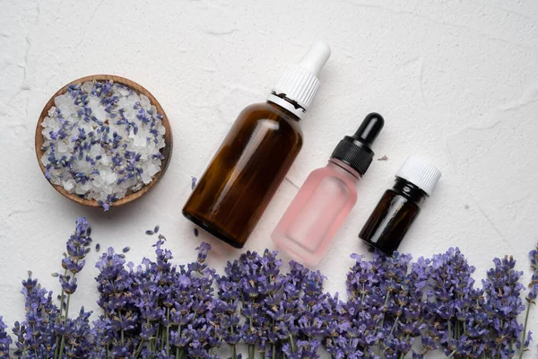 Dry lavender flowers, salt, seeds and bottles of essential lavender oil for skin care on white concrete background. Flat lay, top view. Copy space
