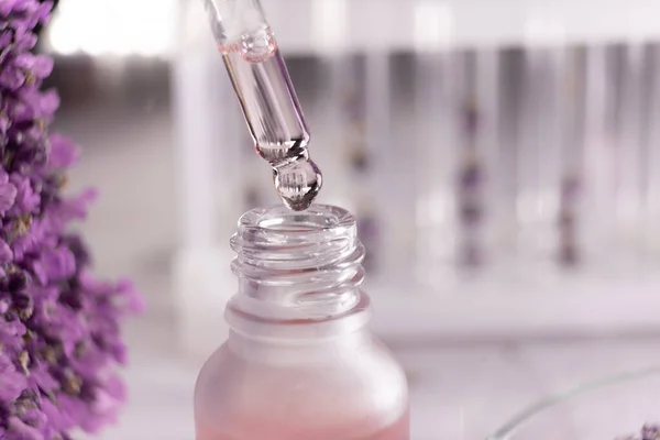 Natural oil dripping into bottle and lavender flowers, close up. Cosmetic product. Copy space