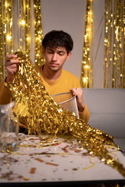 Man cleaning foil curtain into trash bin after New Year\'s Eve party. Copy space