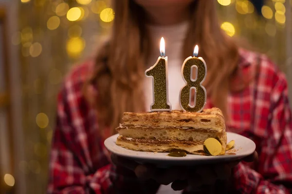 Young woman blowing out candles 18 on birthday cake. Eighteen birthday concept. Copy space