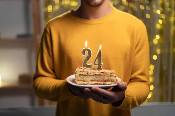 Cake with the number 24 lighted candles in men hands. 24th birthday concept