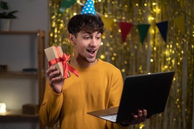 Doğum günü hediyesini dizüstü bilgisayarla alan, doğum gününü evde uzaktan arkadaşlarıyla kutlayan bir adam. Mesafeli tatil kutlaması, sanal parti konsepti. Boşluğu kopyala