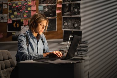 Dedektif geceleri dizüstü bilgisayarla ofiste delil incelerken. Boşluğu kopyala