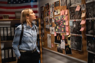 Policeman analyzing information of crime on investigation board, detective professional working in her office. Copy space