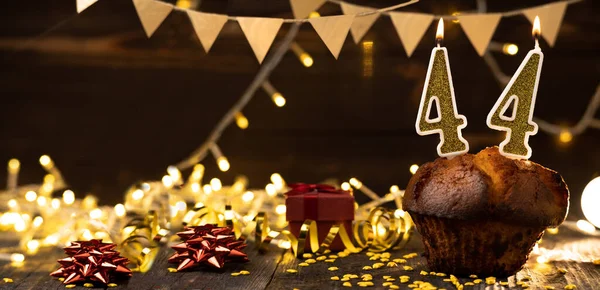 Number 44 golden festive burning candles in a cake, wooden holiday background. forty four years from the date of birth. the concept of celebrating a birthday, anniversary, holiday. Banner. copy space