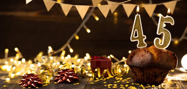 Number 45 golden festive burning candles in a cake, wooden holiday background. forty-five years from the date of birth. the concept of celebrating a birthday, anniversary, holiday. Banner. copy space