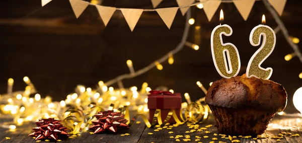 Number 62 golden festive burning candles in a cake, wooden holiday background. sixty-two years of birth. the concept of celebrating a birthday, anniversary, holiday. Banner. copy space