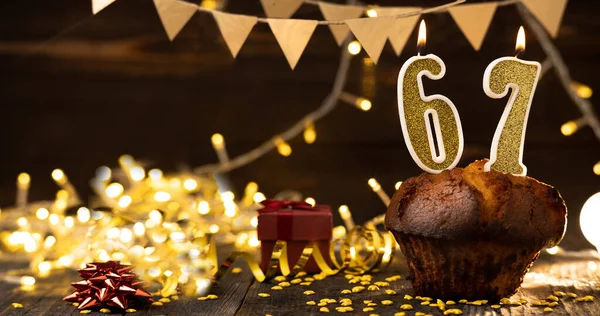 Number 67 golden festive burning candles in a cake, wooden holiday background. sixty-seven years of birth. the concept of celebrating a birthday, anniversary, holiday. Banner. copy space
