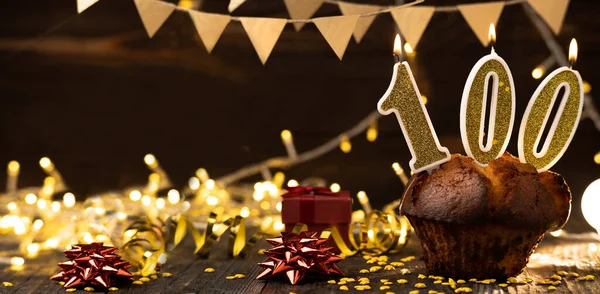 Number 100 golden festive burning candles in a cake, wooden holiday background. hundred years since the birth. the concept of celebrating a birthday, anniversary, holiday. Banner. copy space