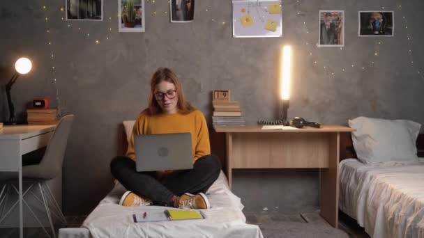 若い美しい白人女子大生が大学の寮の部屋のベッドに座って ラップトップを使ってビデオ通信で通信しています 愛する人とのビデオ通話 コピースペース — ストック動画