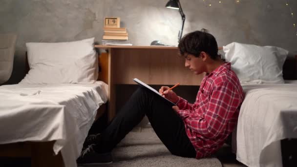 一个少年学生坐在大学宿舍的地板上 在笔记本里翻阅摘要并做笔记 复制空间 — 图库视频影像