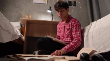 a young Arab student sits at night on the floor in a hostel among open paper books looking for the necessary information. The concept of preparing a homemade creative task. copy space.