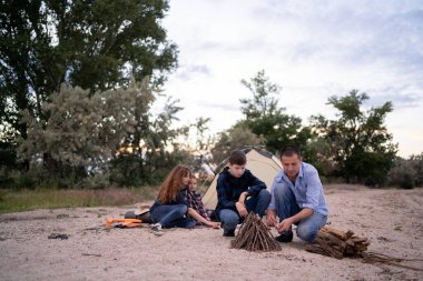 Camping on the beach. The family is resting making a campfire at sunset. Dad and son spend time together in nature. Copy space