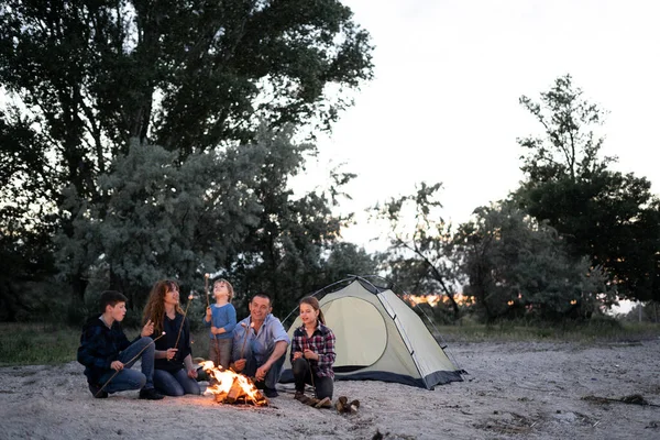 Happy family roasting marshmallow over campfire near tent. Camping, hike and people concept