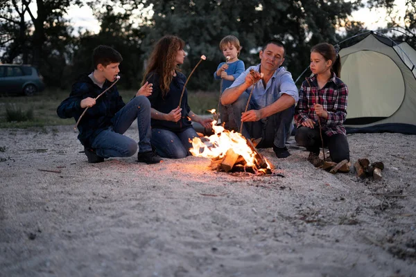 Family grilling marshmallows in the evening on beach. Copy space