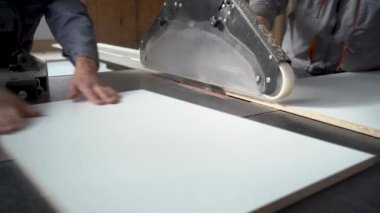 hands of carpenters working with a sliding panel saw and sawing wood fiber board in a furniture factory or chipboard workshop. the concept of production, fabrication and woodworking industry