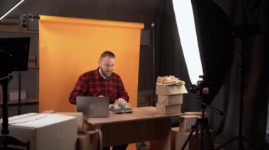 a young business owner is sitting in a home video studio recording a review of goods for an online store. looks into the camera makes a test drive of sports shoes. Business social media influencer.