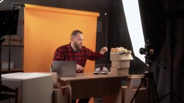 Ev video stüdyosunda turuncu arka planda küçük ve orta büyüklükte bir erkek satış elemanı online spor ayakkabıları mağazası için video eleştirisi yapıyor. İş dünyası sosyal medya etkileyiciName.