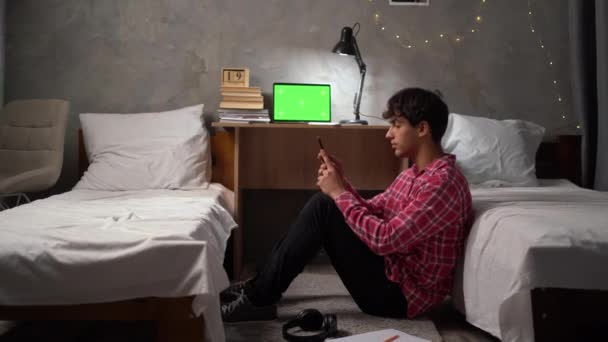 若いアラブの学生は 大学の寮で夜に床に座って ヘッドフォンをつけ スマートフォンで音楽をオンにし 耳を傾け リラックスします 訓練の後で休みなさい コピースペース — ストック動画