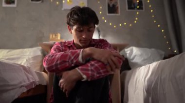 A young arab student sits on the floor in depression in a college dormitory hugging his knees with his hands. Sad man, crying, drama, lonely and unhappy concept. copy space.