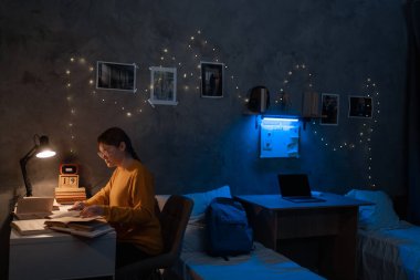 Girl college student studying in dormitory reading books at late night in bedroom. Copy space