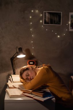 Tired college student sleeping at table in dormitory preparing for exam at night. Copy space