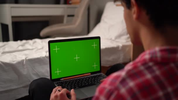 在一个大学生宿舍里的一个男生手里的特写镜头 他在用一个带有绿色屏幕模型的笔记本电脑上工作 在网上与朋友聊天 — 图库视频影像