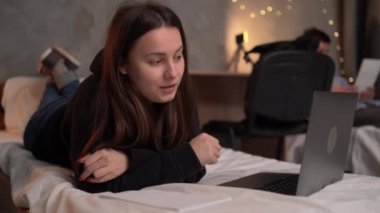 close-up portrait of a young teenager girl student lies on a bed in a college dormitory at night makes a video call. copy space. real authentic life