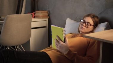 A college student is studying on the bed, a young girl is lying and reading her notes in a notebook making notes with a pen. copy space.