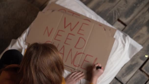 一个在大学宿舍里的女权运动者晚上坐在床上 写着一张海报 上面有红色记号 我们需要零钱 准备抗议行动的概念 从上往下看 — 图库视频影像