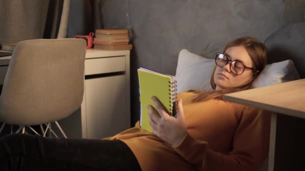 一个大学生在床上学习 一个小女孩在撒谎 在笔记本上用钢笔记笔记 复制空间 — 图库视频影像