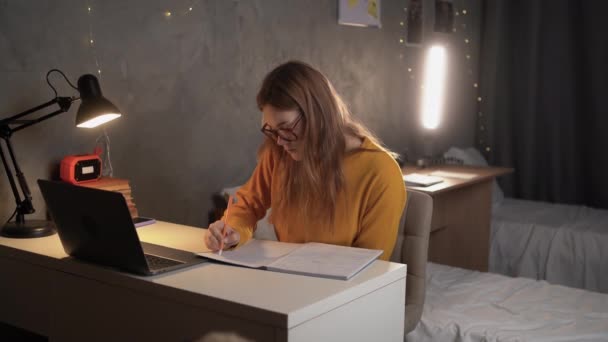 十几岁的女生坐在大学宿舍的一张桌子旁 用笔记本电脑和笔记本里的笔记在网上查找信息 复制空间 — 图库视频影像