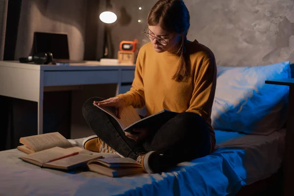 Serious female college student studying in dormitory preparing for exam at late night. Copy space