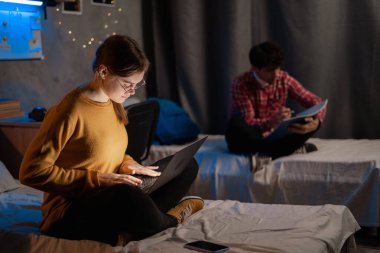 Students girl and guy studying in college dormitory at night. Student use laptop computer in dark domestic room. Copy space