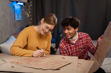 Teenage activists draw posters for a protest action for protecting the planet against global warming while sitting in a dorm room. Copy space