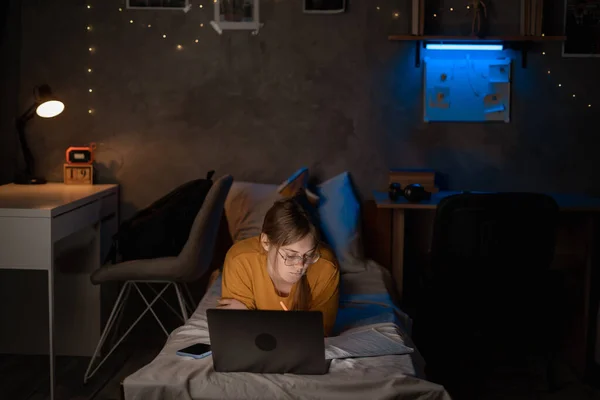 Girl student studying at night in dormitory using laptop computer on bed. Copy space