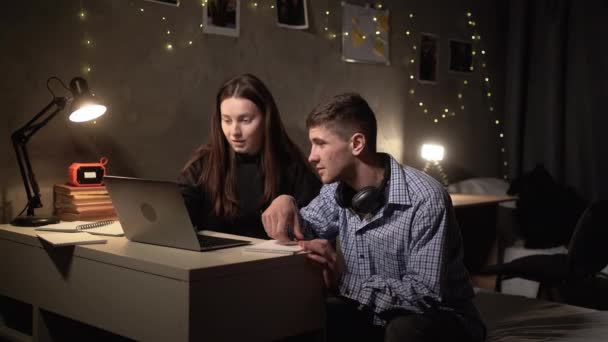 两个年轻人晚上坐在旅馆的餐桌前 准备着一项创造性的任务 紧张地讨论着什么 搜索笔记本电脑上的信息 — 图库视频影像