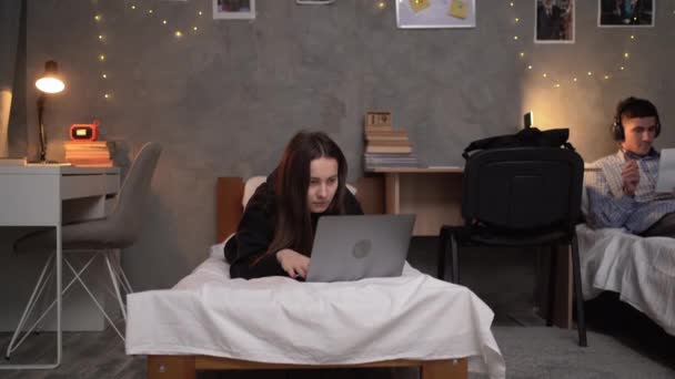 若い10代の女の子の学生は 彼女のラップトップを使用してオンラインで情報を探している夜に大学の寮のベッドの上にあります コピースペース — ストック動画