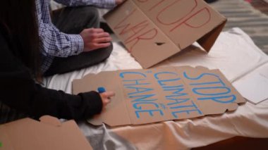 close-up of the hands of the activists are preparing a poster. The words stop climate change are written on paper.