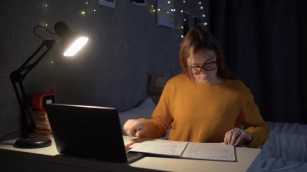 十几岁的女生坐在大学宿舍的一张桌子旁 用笔记本电脑和笔记本里的笔记在网上查找信息 复制空间 — 图库视频影像