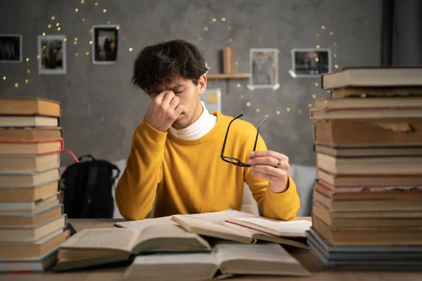Attractive man with eyeglasses in hand. Poor young guy has issues with vision. He rubs his nose and eyes out of fatigue. Male student tired to study and read books. Copy space