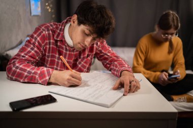 Serious college student taking notes in notebook studying in dormitory. Dorm education concept