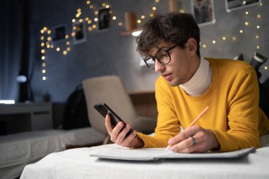Arabic young guy college student holding smartphone studying on cell, distance learning using apps for education, e learning on mobile phone in university campus at night. Copy space