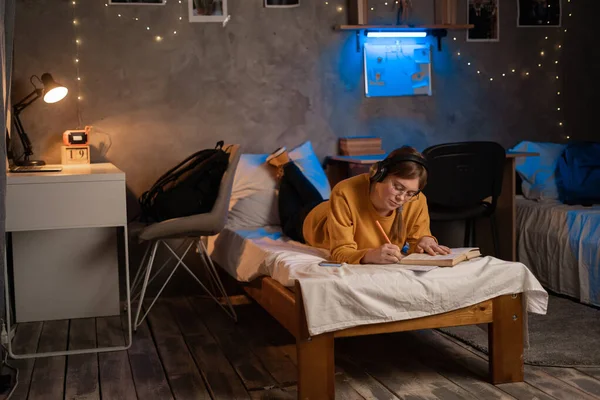 Female university or college student studying with textbooks on bed in dorm room. Night life of student. Copy space
