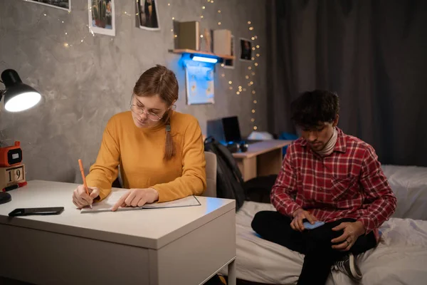 Serious female and male college students studying in dormitory at night. Copy space