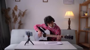 Practicing guitar music happy young male musician using smartphone software applications for learning at home. Copy space