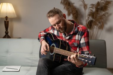Practicing in playing guitar. Handsome man learning playing guitar at home in the evening. copy space